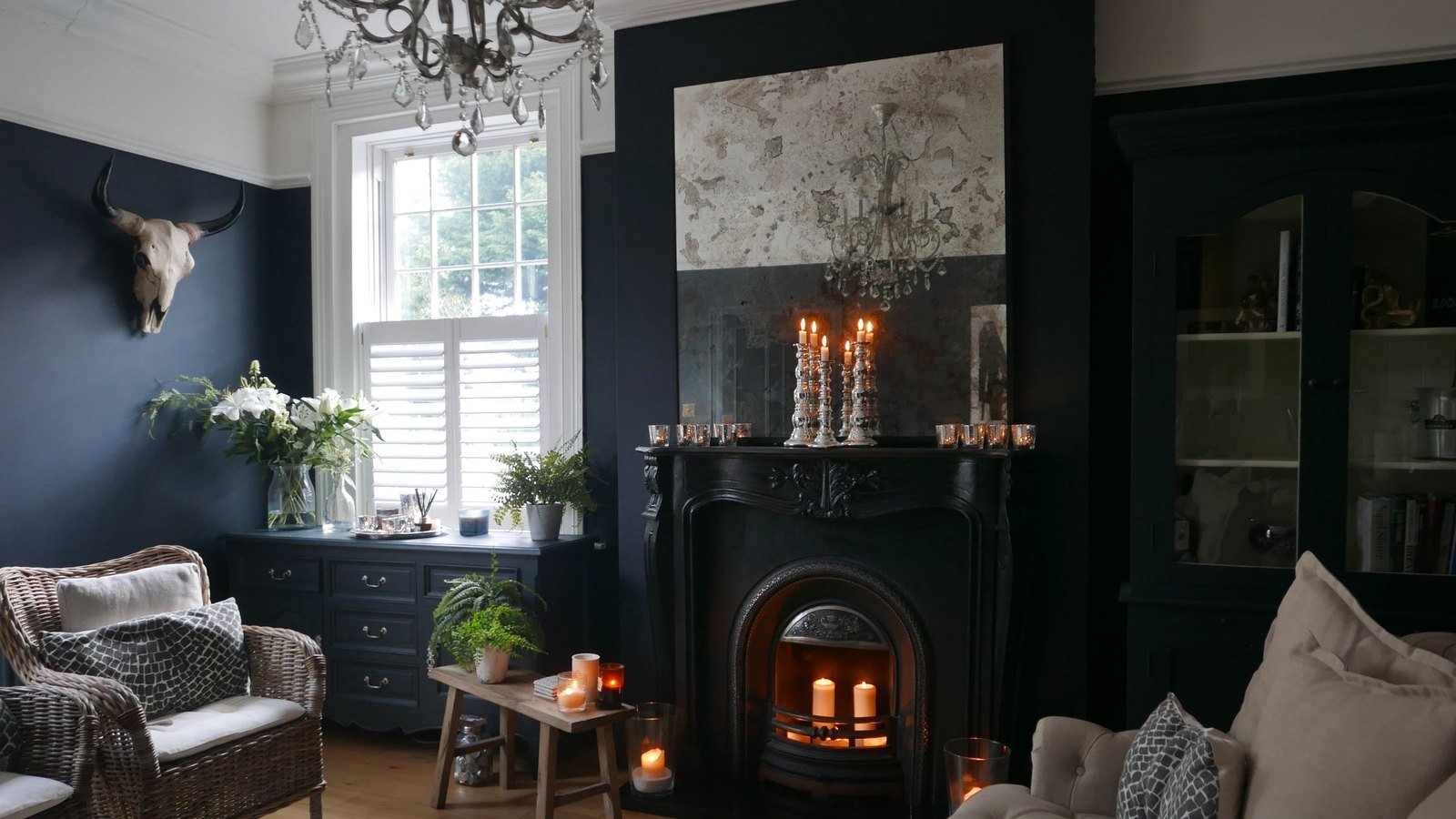 Reference photograph of a navy living room with a candle-lit fireplace, wicker armchairs and a tufted sofa